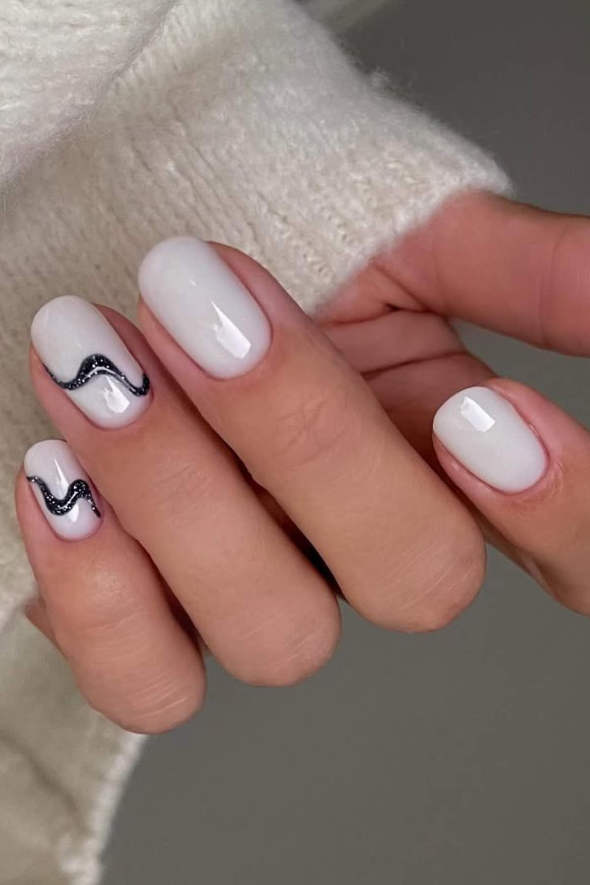 A hand with short, almond-shaped white nails; two nails feature a black wavy line design.