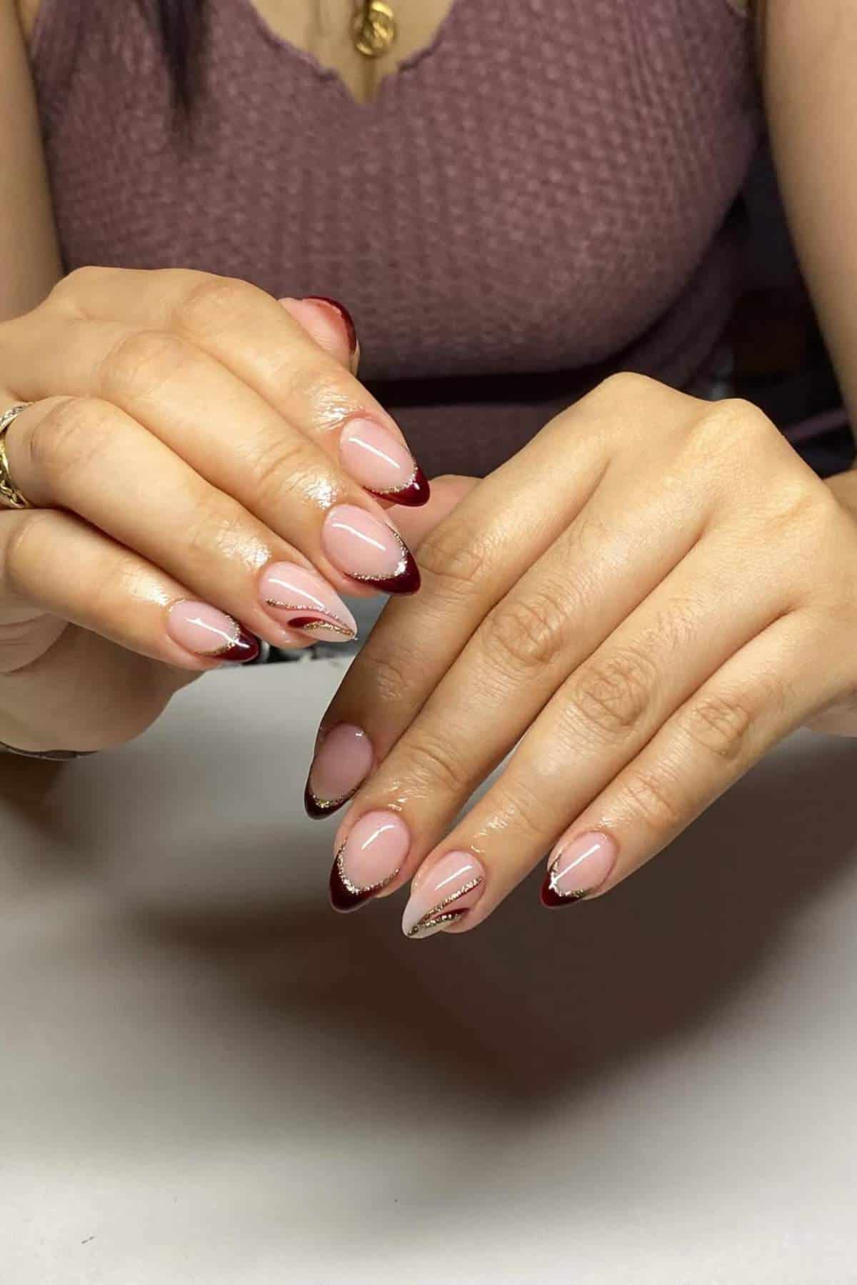 A person with almond-shaped nails featuring a nude base, burgundy French tips, and silver accent lines on some nails.