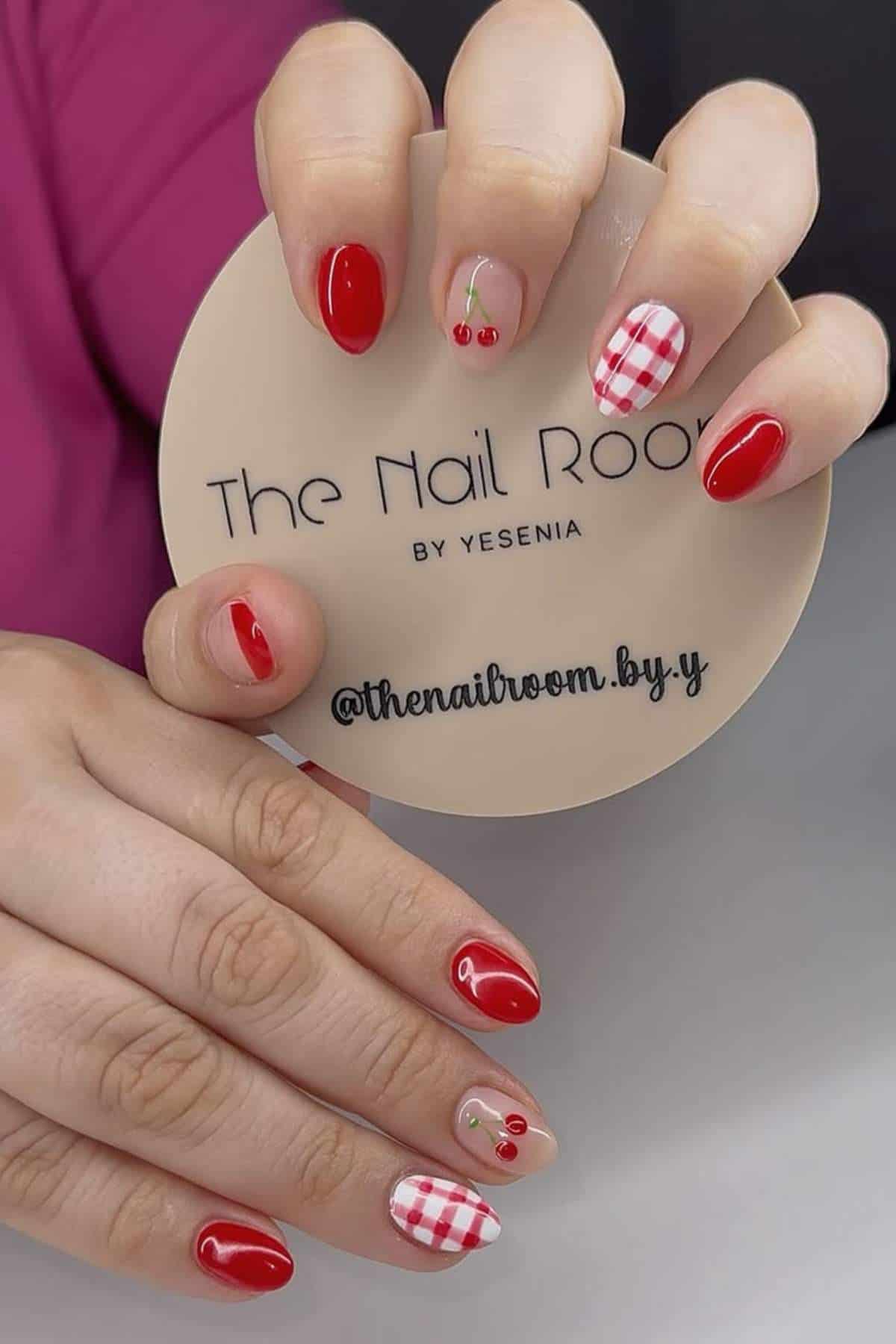 A hand with red, cherry, and red-and-white checkered nail art holds a beige sign that reads "The Nail Room by Yesenia.