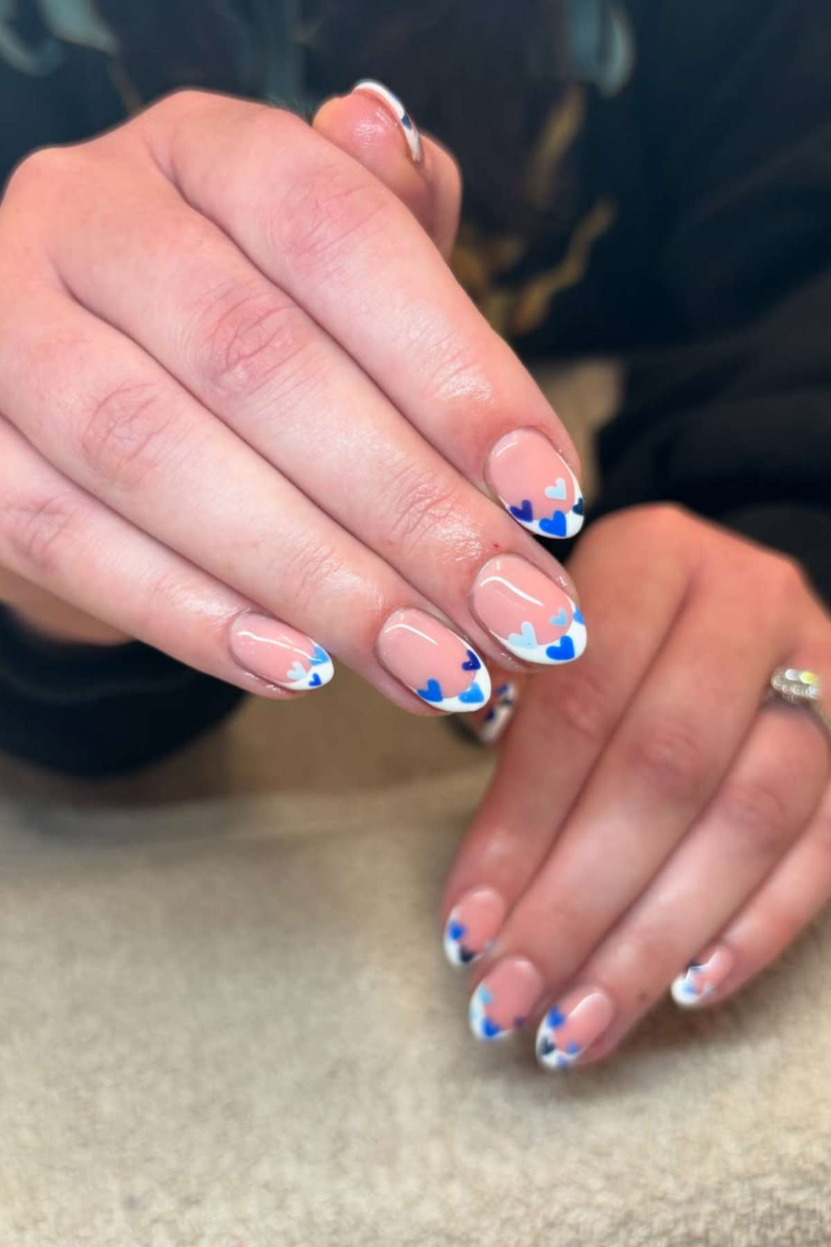 Close-up of hands showing manicured nails with a nude base, white tips, and small blue heart designs on each nail.