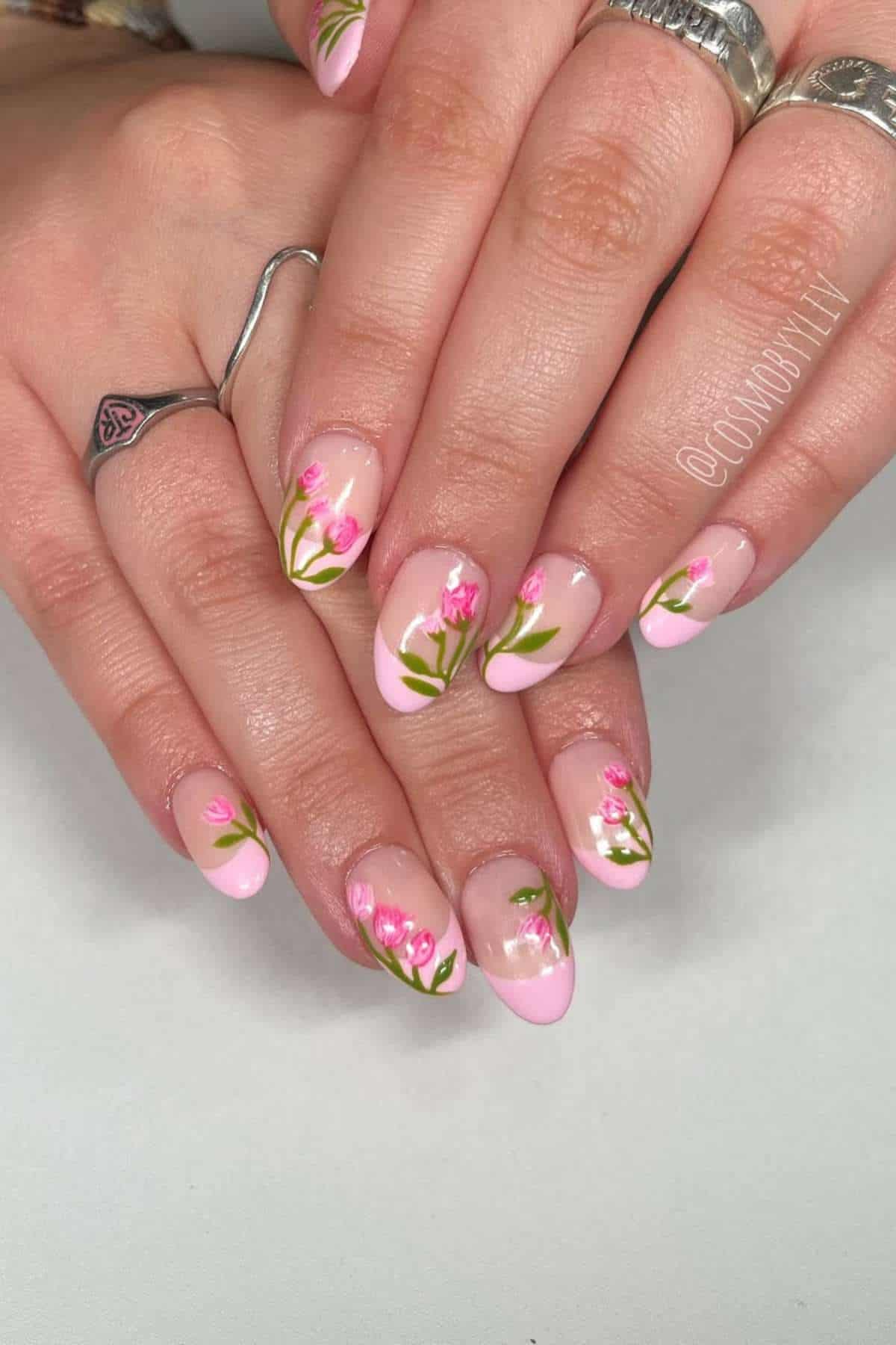 Hands with manicured nails featuring light pink tips and small hand-painted floral designs, set against a plain background.
