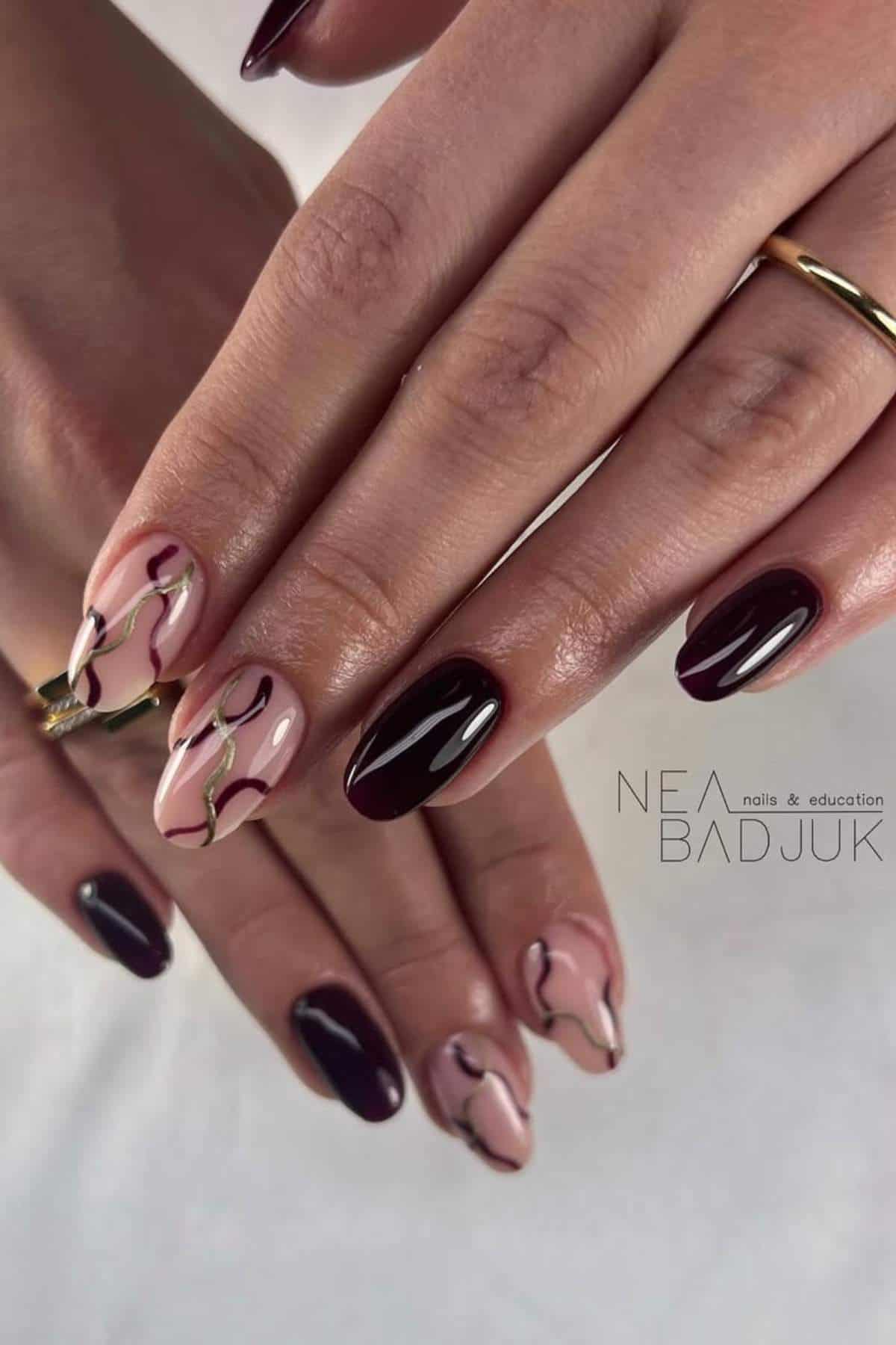 Hands with manicured nails; some nails are painted dark burgundy, while others have a pink base with abstract wavy designs in burgundy and gold.