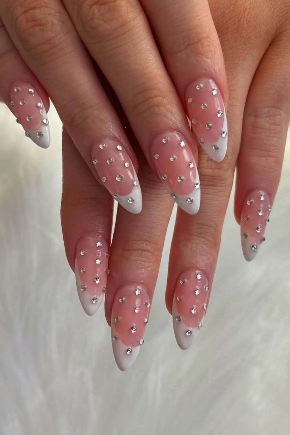 Hands with long, almond-shaped nails featuring a white French tip and small silver rhinestone accents on a light pink base.