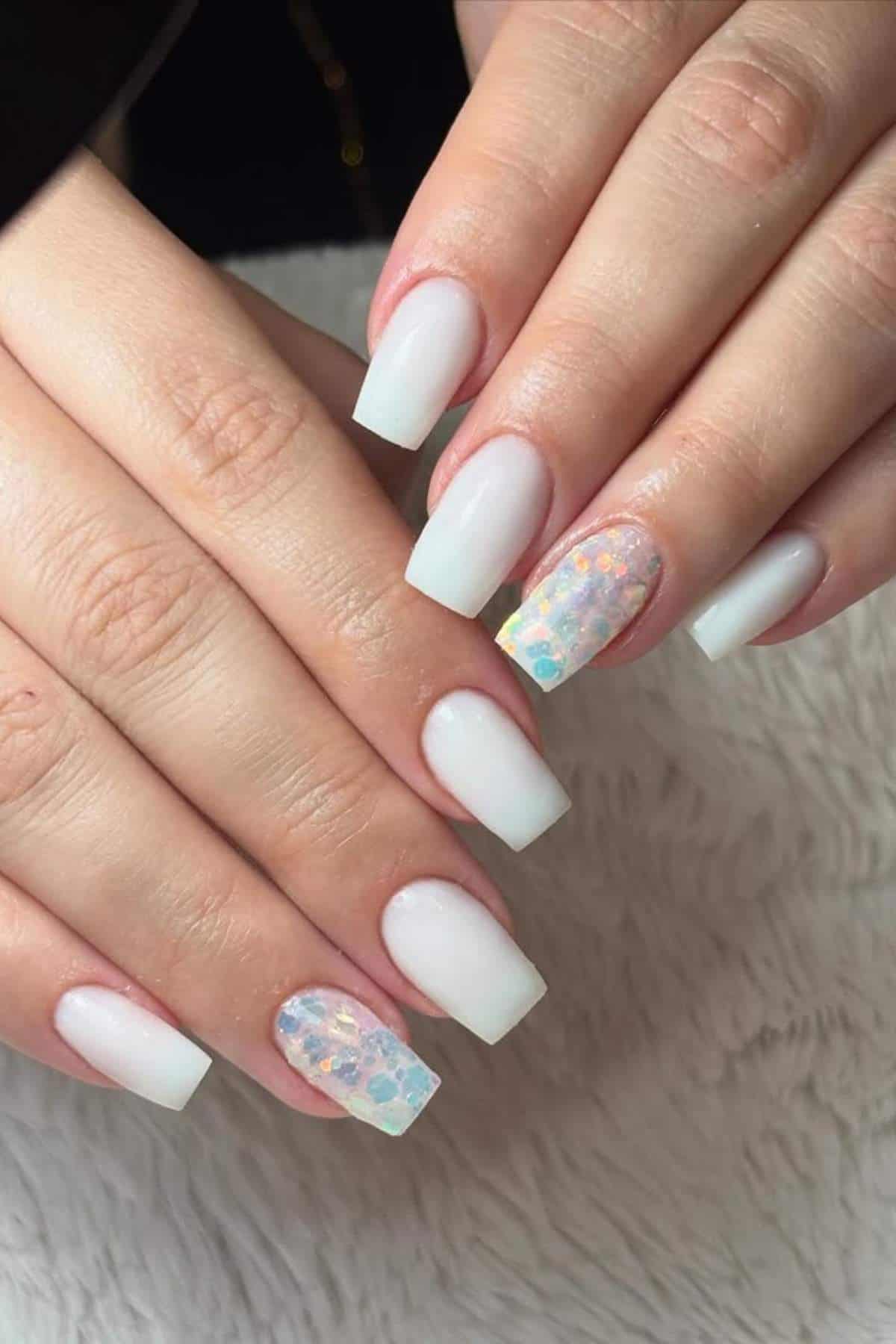 Hands with square-shaped white ombre acrylic nails; ring fingers feature iridescent hexagonal glitter accents.