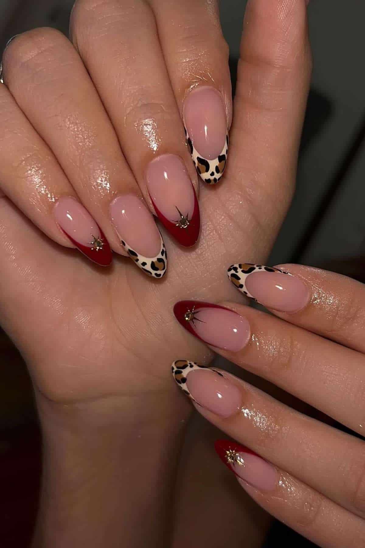 Hands with almond-shaped nails featuring a mix of red tips, leopard print tips, and small gold star embellishments on a nude base.