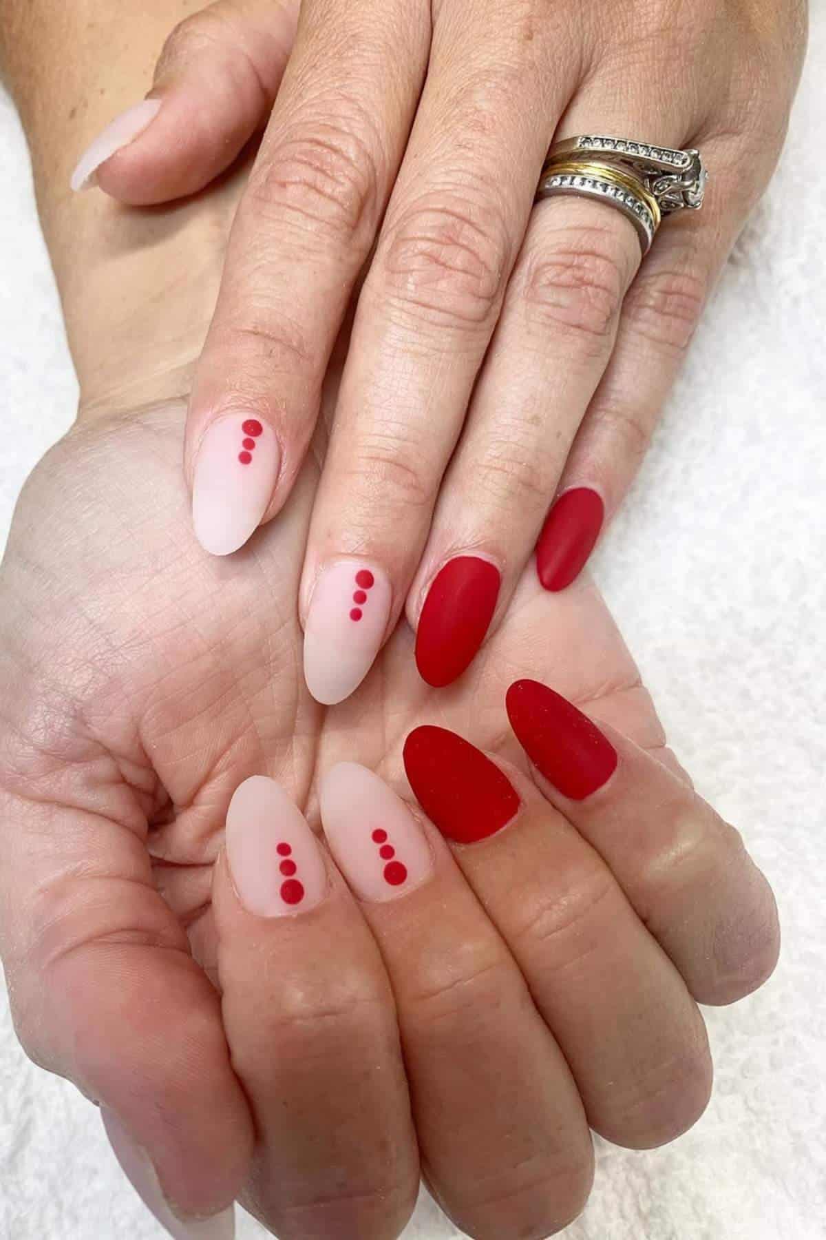 Hands with almond-shaped nails, painted in matte red and pale pink with red dot accents. The person is wearing gold rings on two fingers.