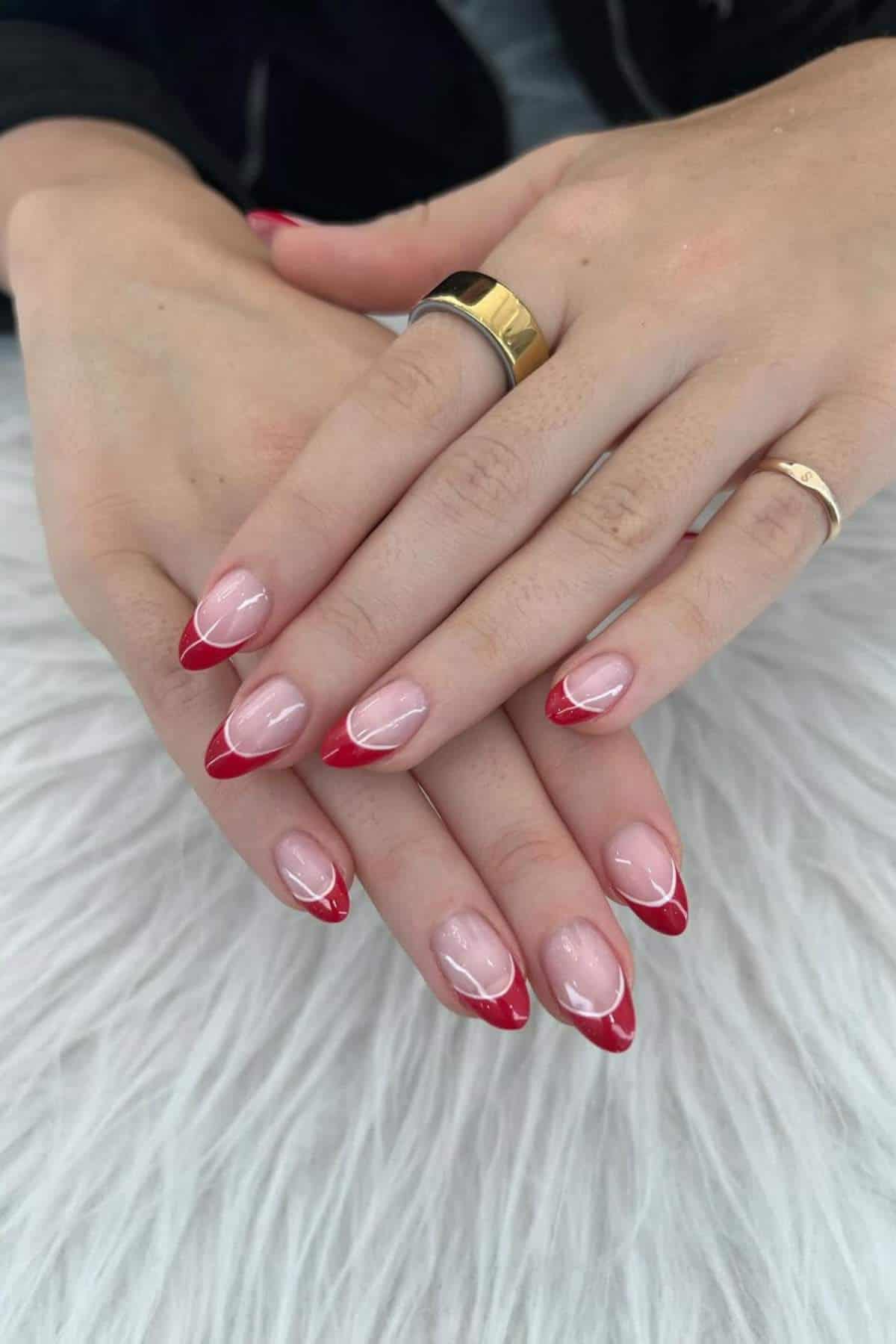 Hands with almond-shaped nails featuring a clear base and red French tip design, resting on a white textured surface.
