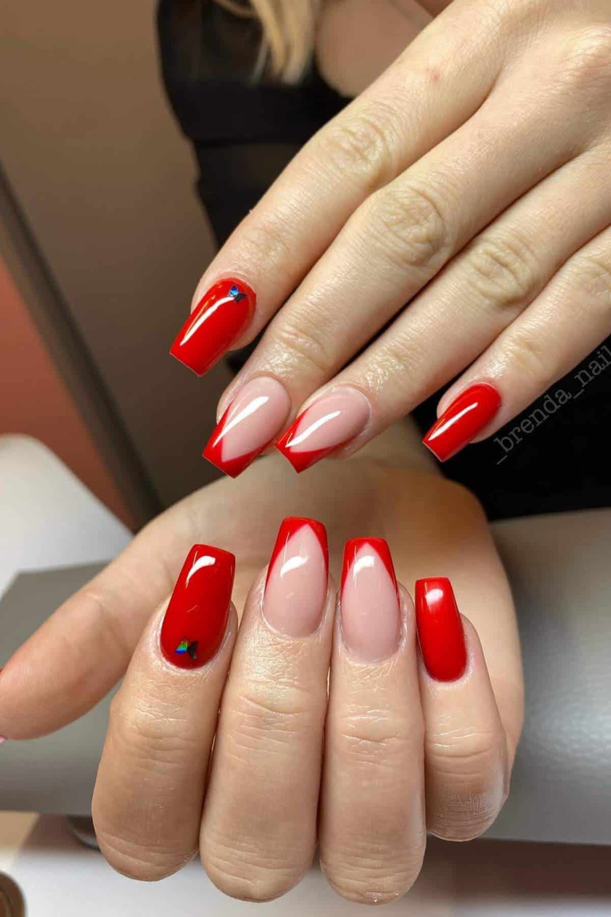 Hands with long, square-shaped nails featuring a red French tip manicure with a glossy finish and a small blue heart detail on one nail.