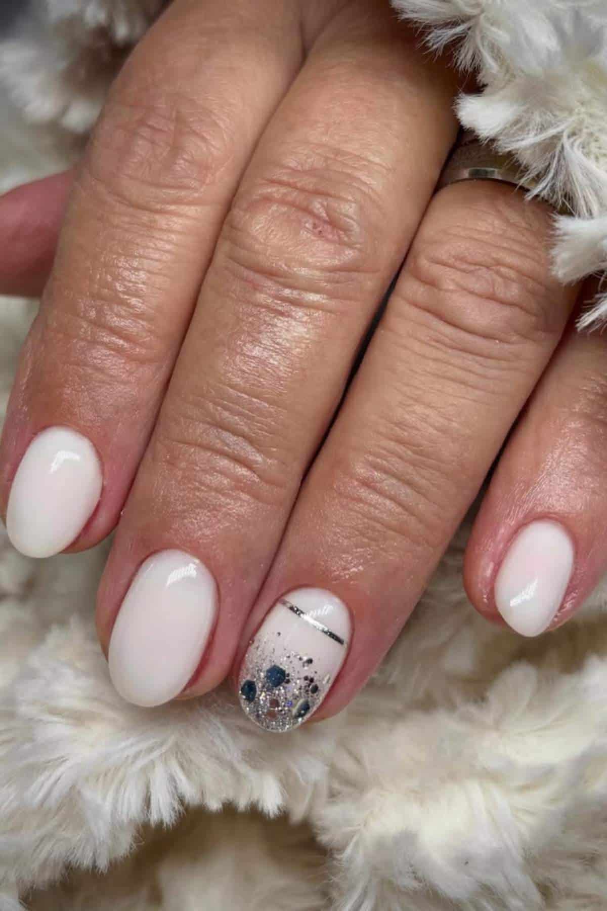 A hand with short, rounded nails painted in a pale pink color; the ring fingernail features silver glitter and black line nail art.