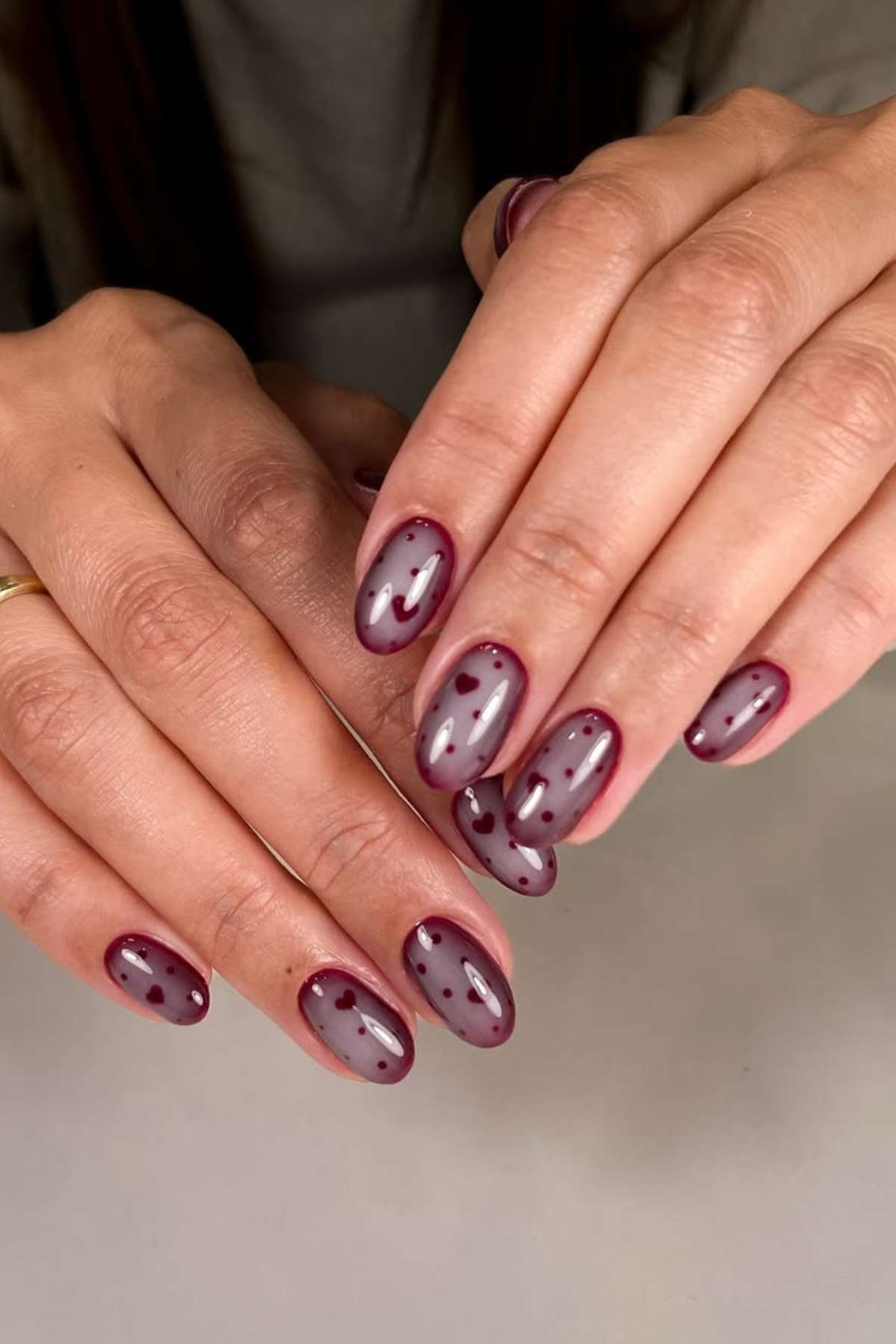 Hands with oval-shaped nails painted in a mauve and burgundy design featuring dots and outlined tips.