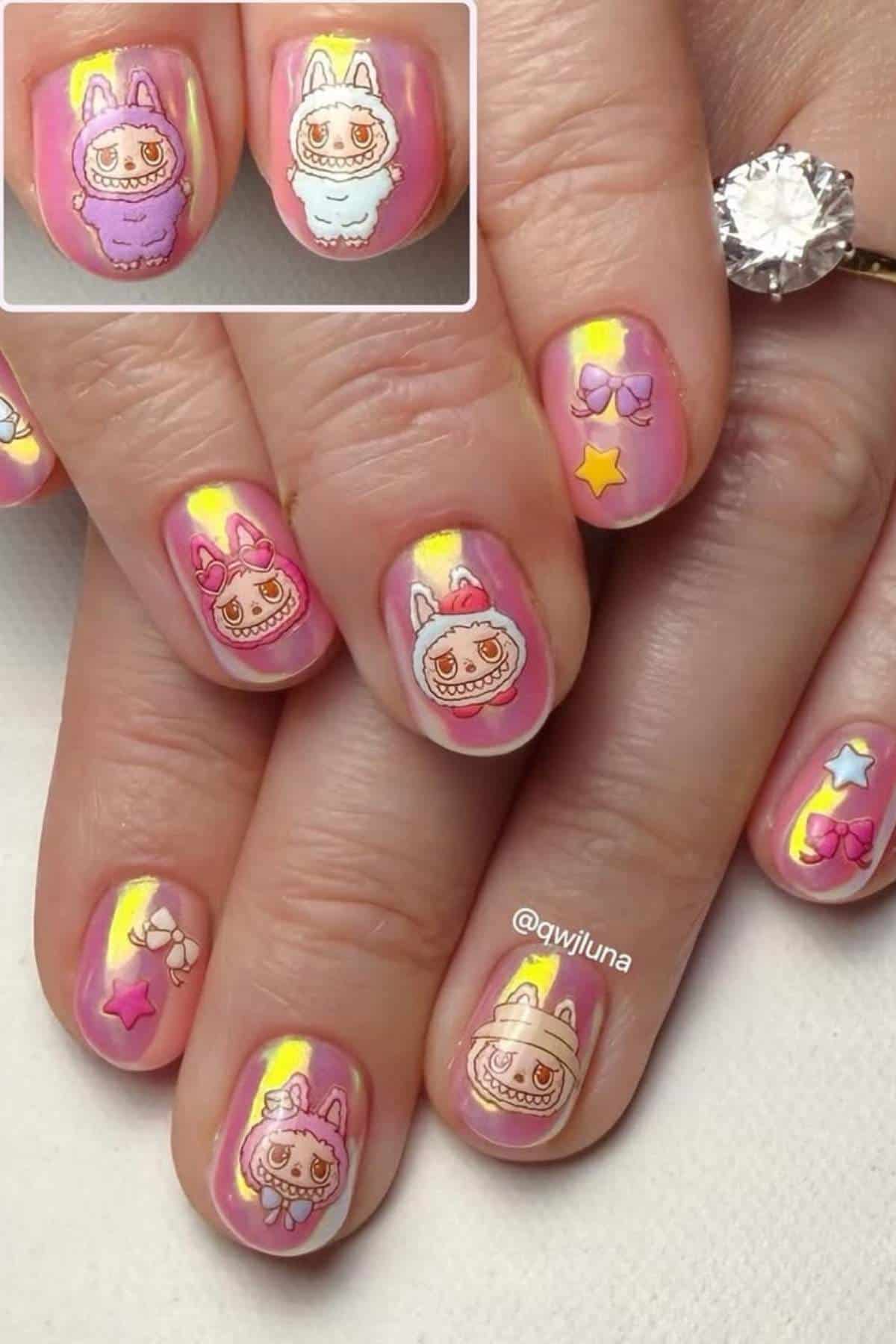Close-up of manicured nails with pink and yellow gradient polish, decorated with cartoon animal faces, bows, and stars in pastel colors.