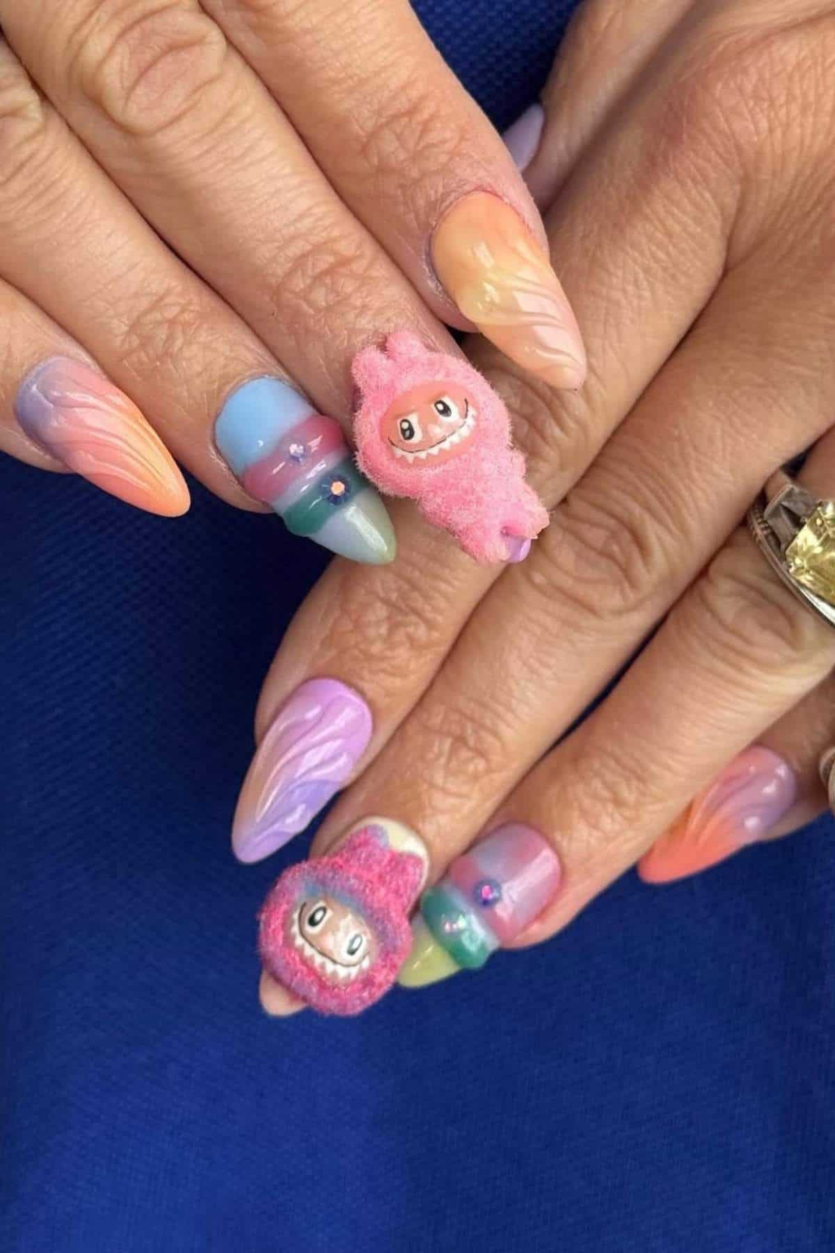 Hands with long, pointed, pastel-colored gradient nails, some nails featuring 3D cartoon character decorations and star-shaped embellishments.
