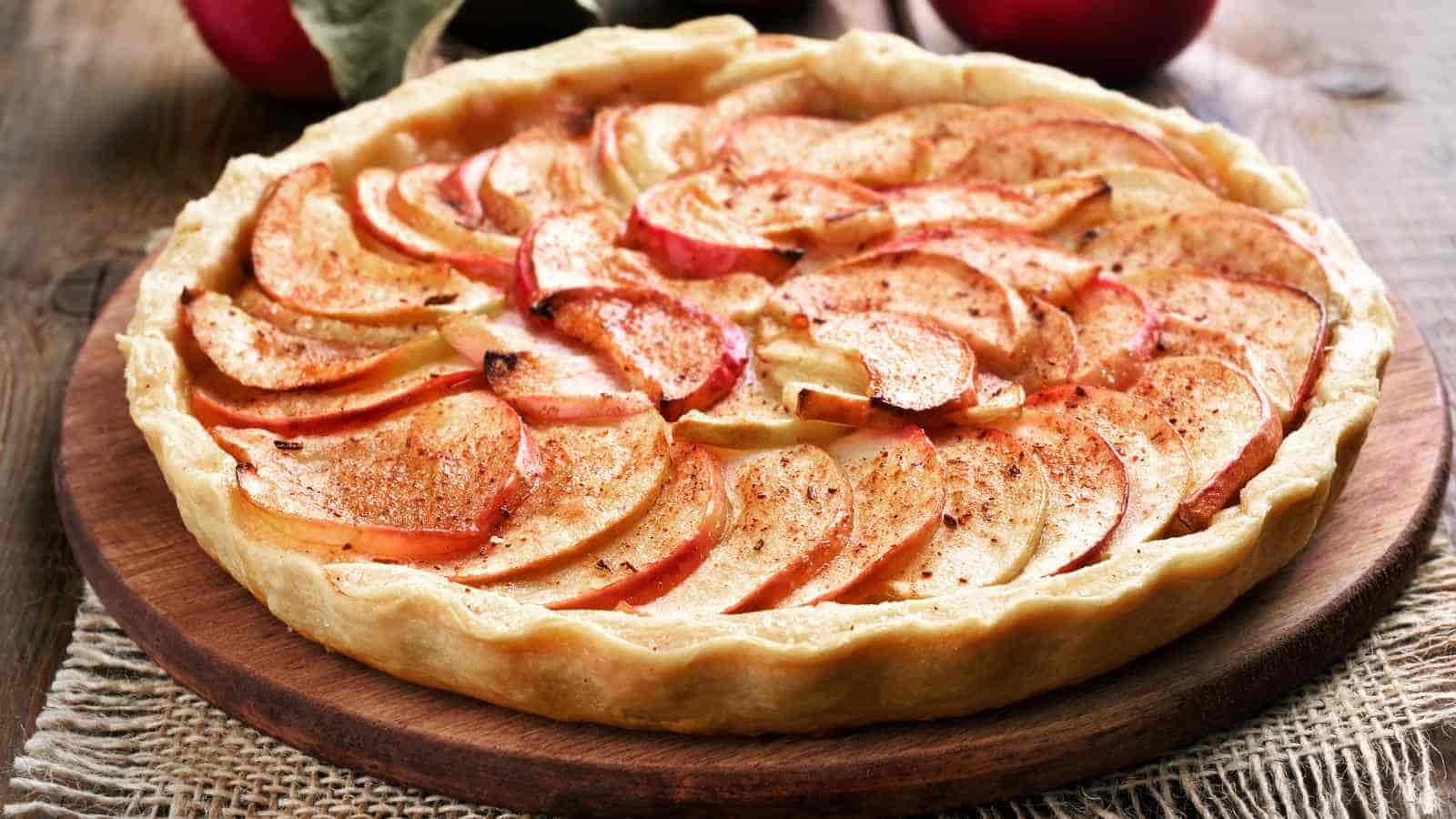 A freshly baked apple tart with a golden crust and neatly arranged apple slices on top, placed on a wooden board.