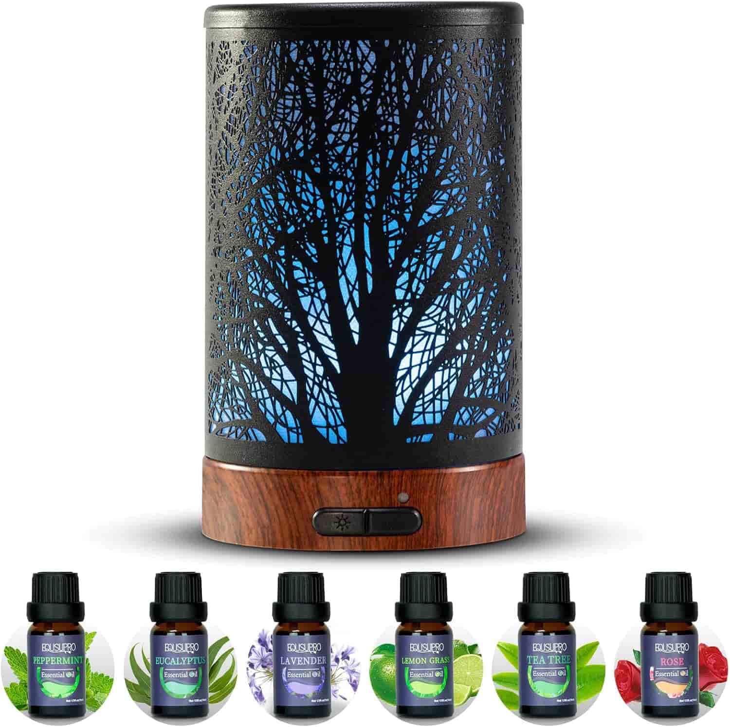 A black metal essential oil diffuser with a tree design and blue light, shown with six bottles of assorted essential oils in front.