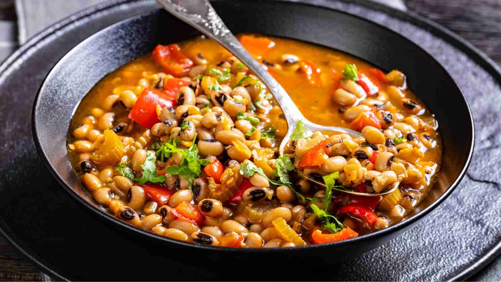 A bowl of black-eyed pea stew with diced tomatoes, celery, and fresh herbs, served with a spoon.