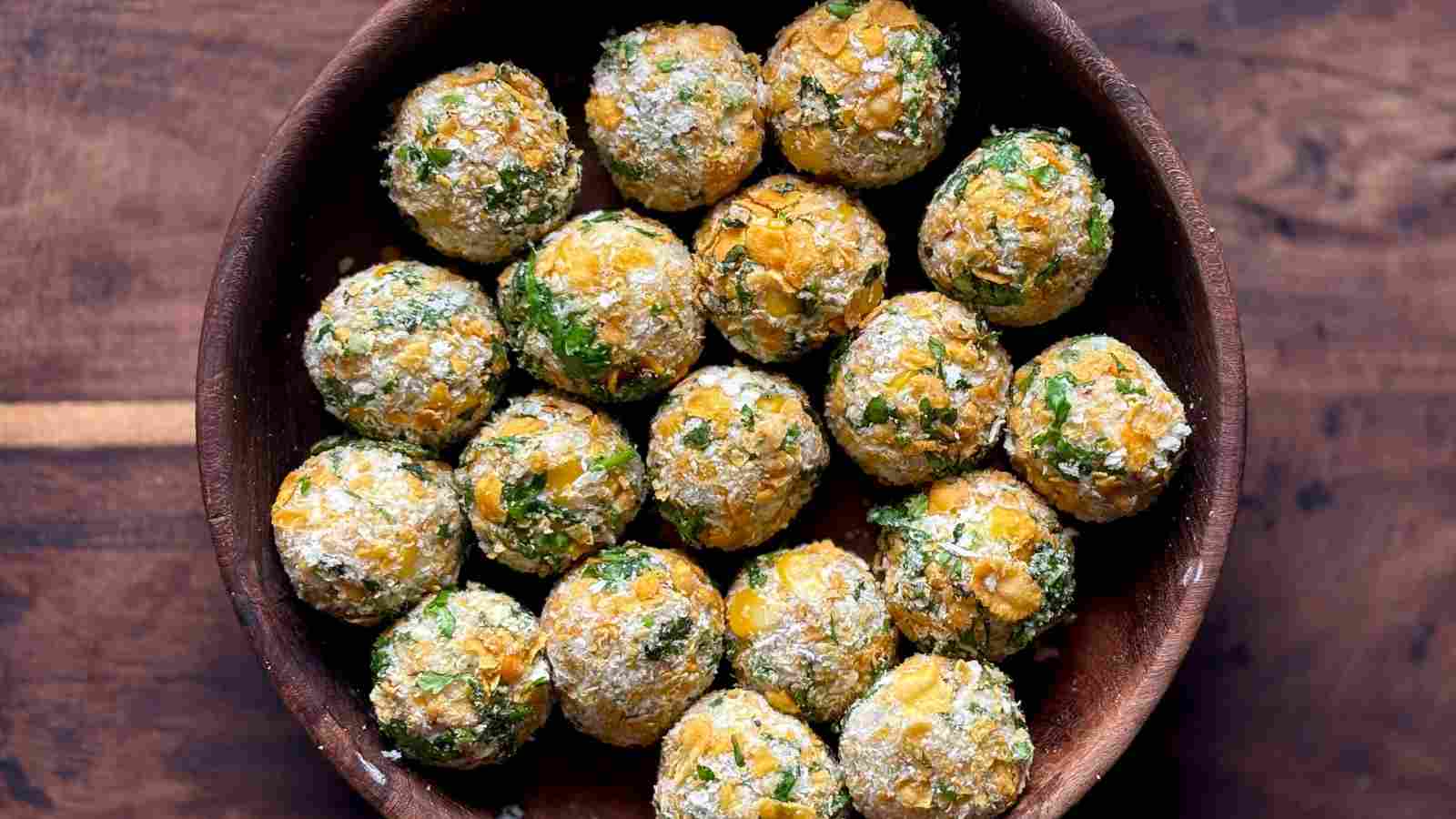A wooden bowl filled with round, uncooked vegetable and herb balls dusted with flour, arranged neatly on a wooden surface.