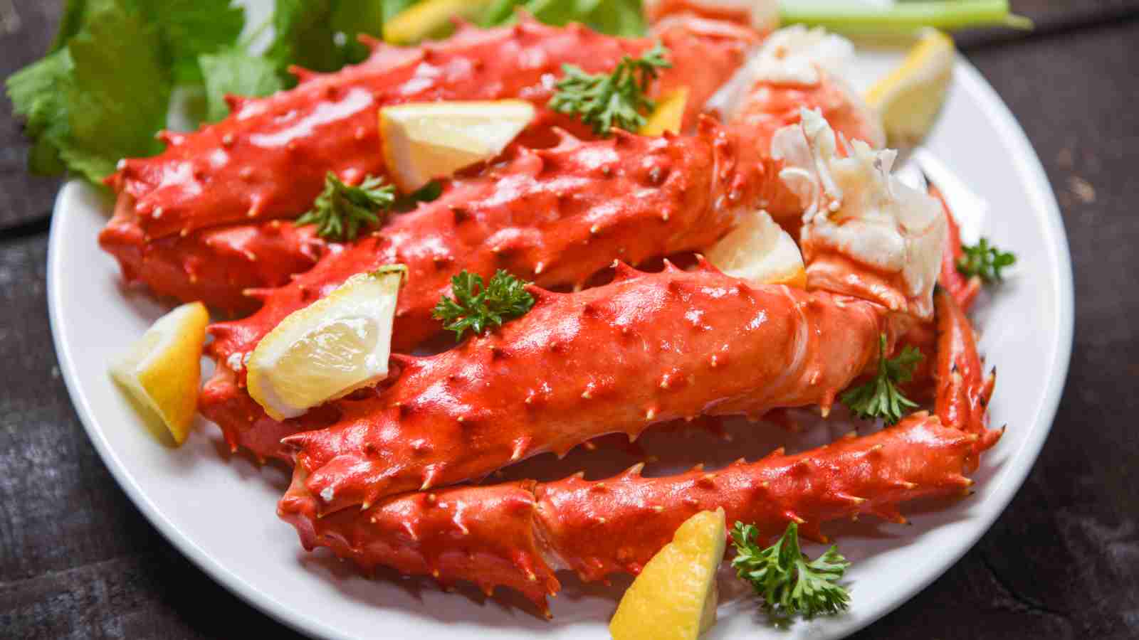 Steamed king crab legs served on a white plate with lemon wedges and fresh parsley.