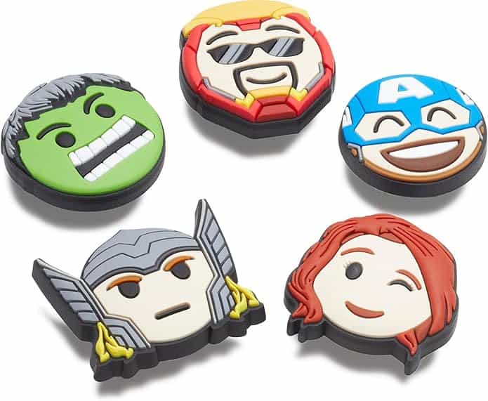Five rubber shoe charms featuring cartoon faces of superheroes, including a green face, a character with a helmet, and others with masks, sunglasses, or red hair, are arranged on a white background.