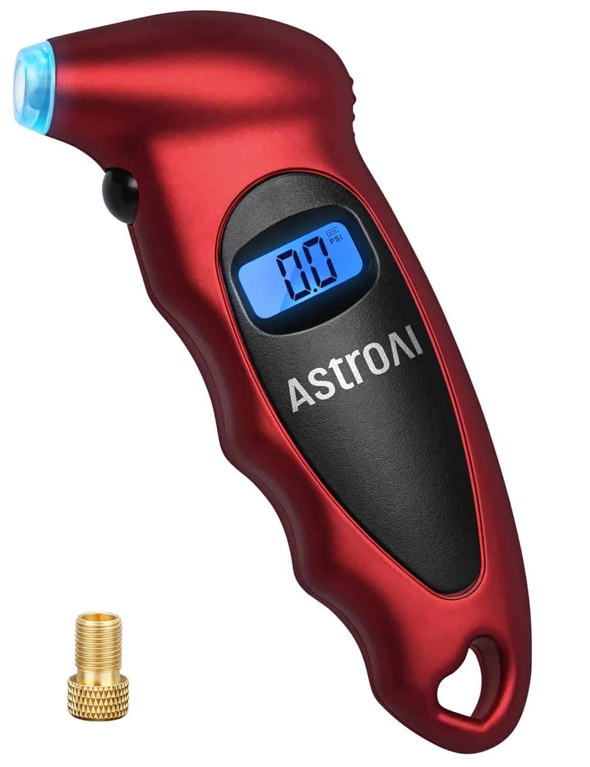 A red AstroAI digital tire pressure gauge with a blue-lit display reading 0.0, shown alongside a brass valve adapter.
