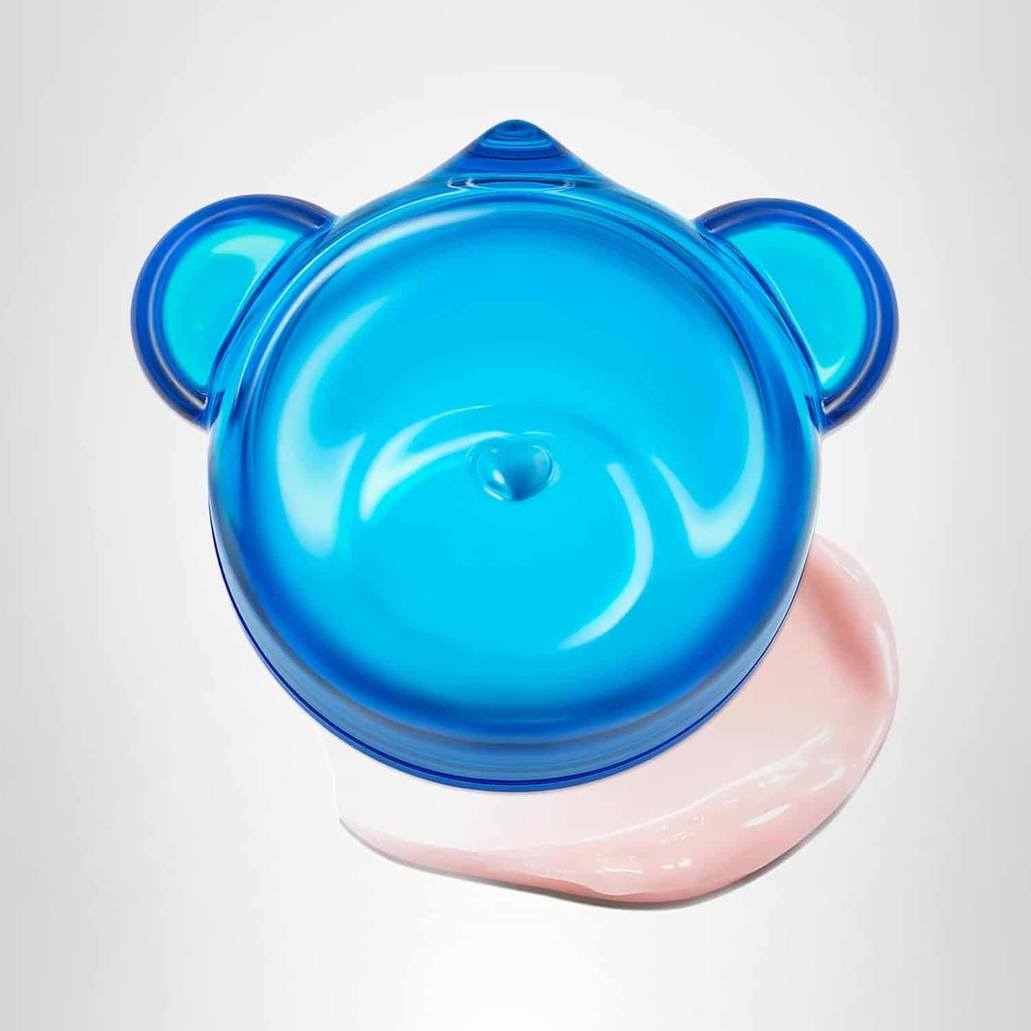 A blue, bear-shaped plastic lid with a swirl design sits on top of a smear of light pink cream against a plain white background.