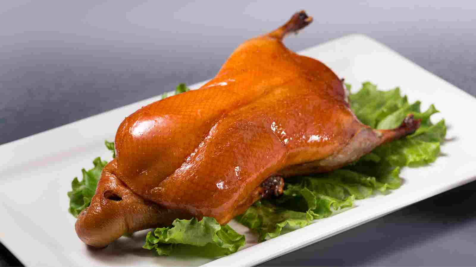 A whole roasted duck served on a bed of green lettuce leaves on a white rectangular plate.