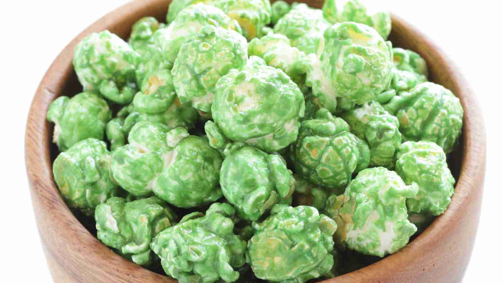 A wooden bowl filled with bright green, candy-coated popcorn against a white background.