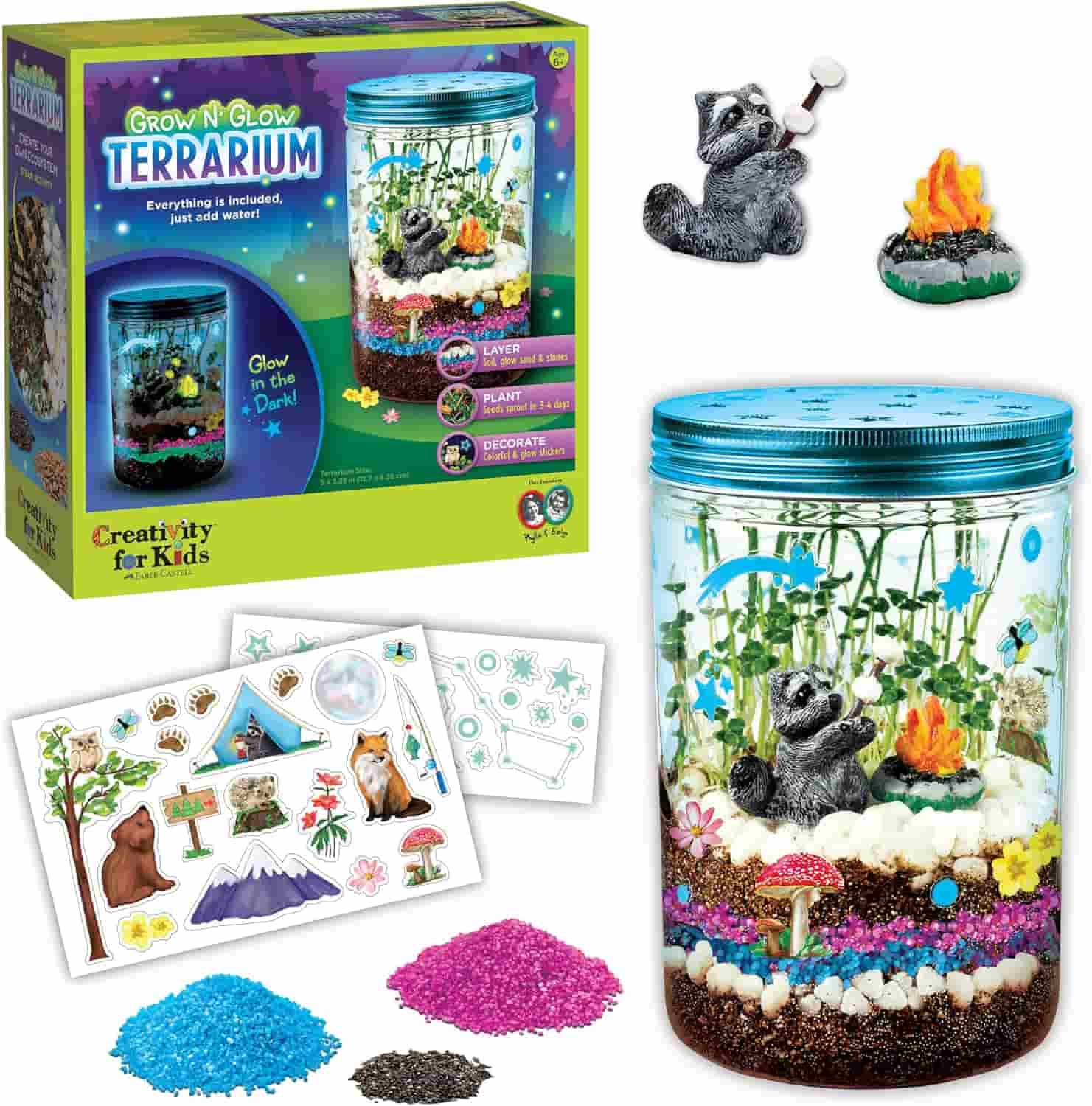 Grown N' Glow Terrarium kit with a decorated jar, raccoon and campfire figurines, colored sand, stones, stickers, and packaging displayed.