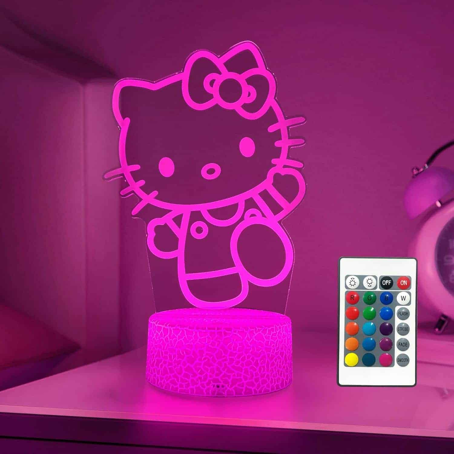 A pink Hello Kitty LED night light on a bedside table, with a multi-colored remote control next to it.