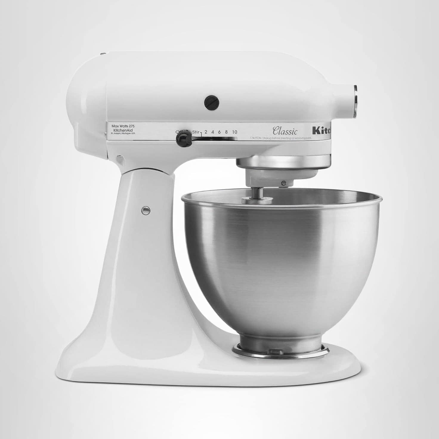 White stand mixer with a stainless steel mixing bowl attached, viewed from the side against a plain light background.