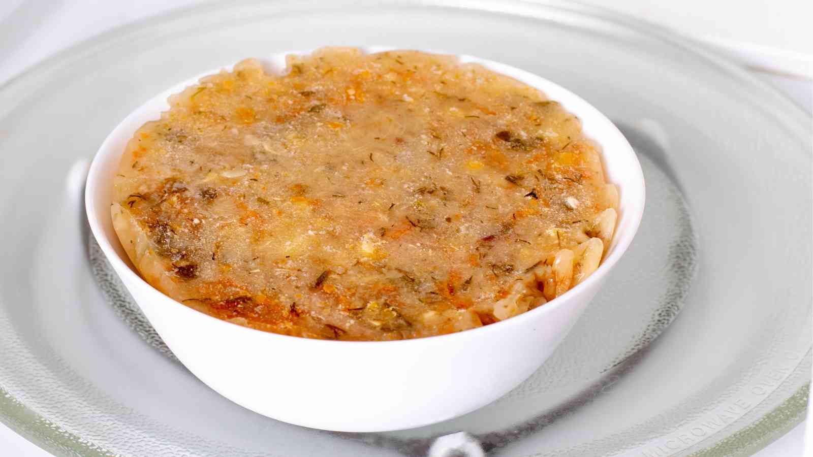 A white bowl filled with frozen pasta and sauce sits on a glass plate, ready to be heated.