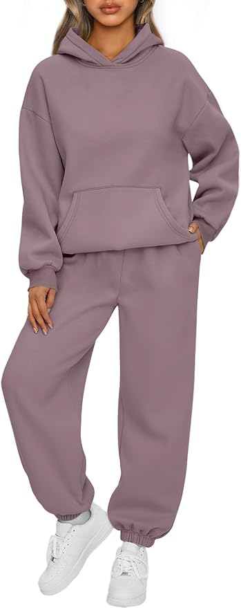 A person wearing a loose-fitting mauve hoodie and matching sweatpants with white sneakers, standing with one hand in the hoodie pocket.