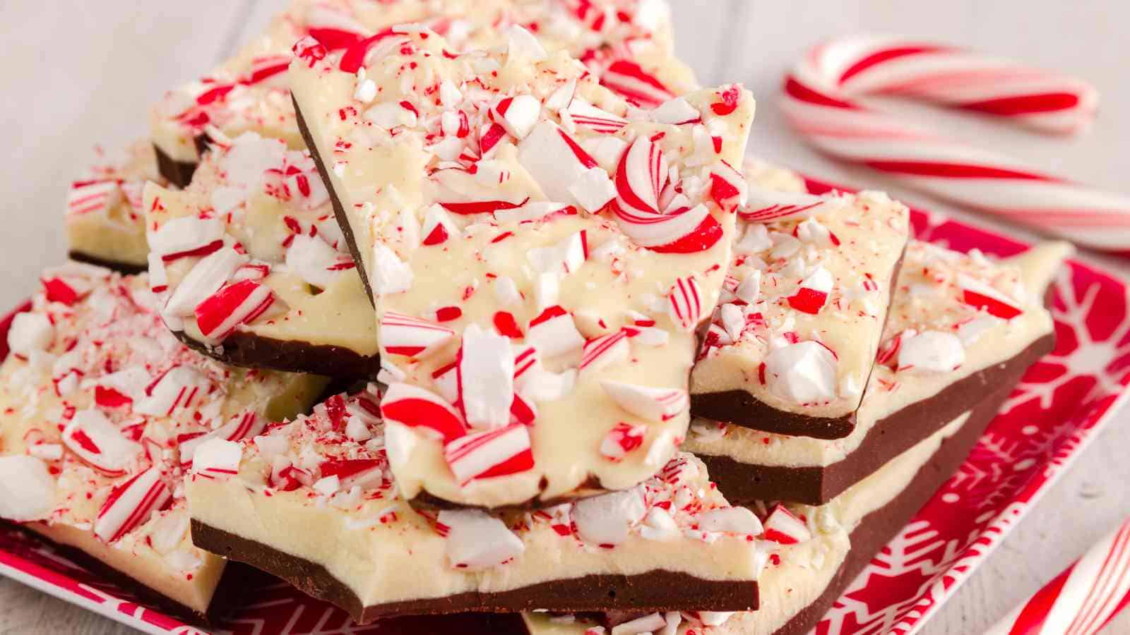 A plate of peppermint bark with layers of dark and white chocolate topped with crushed candy canes, with two candy canes in the background.