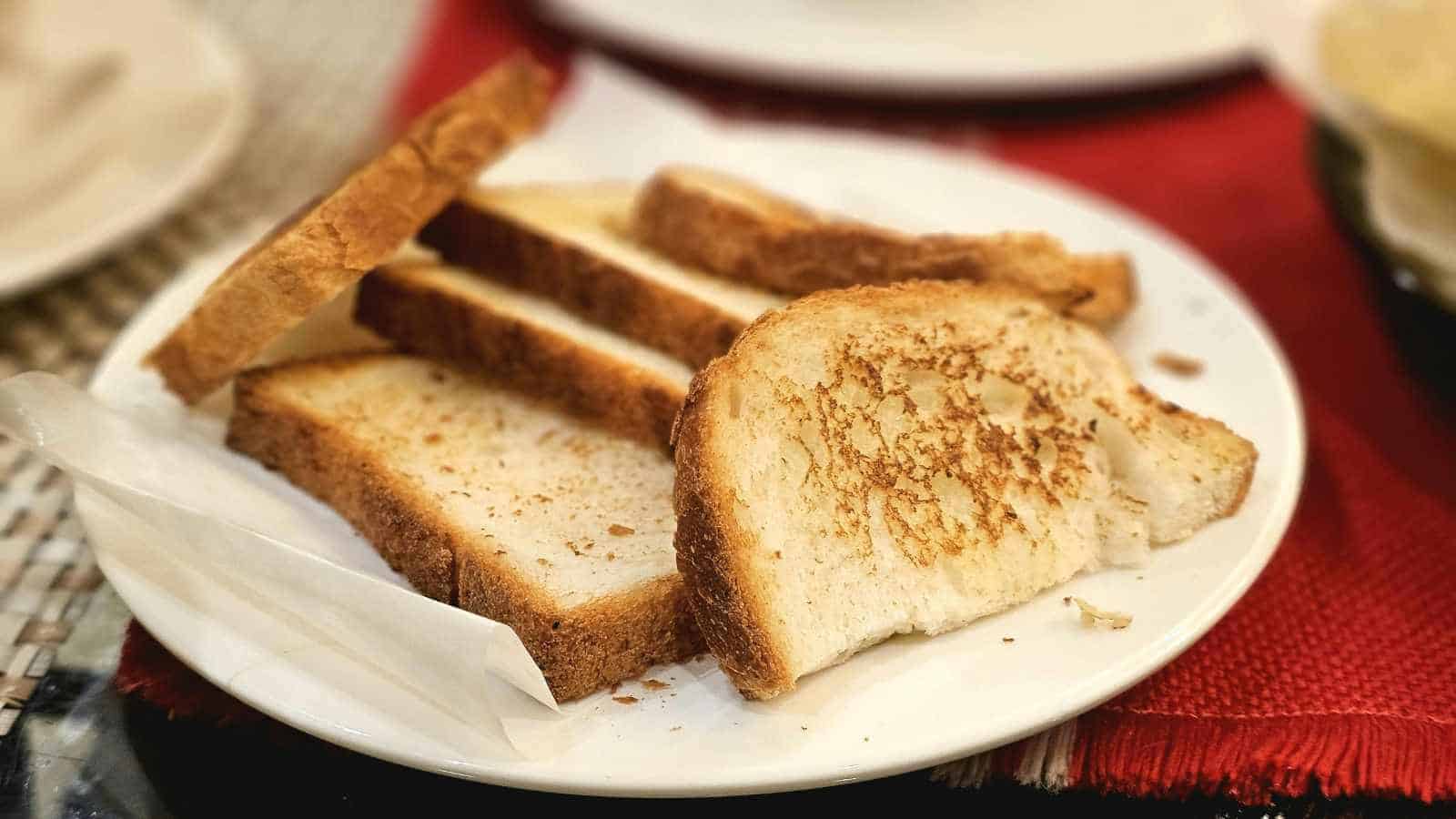 A white plate with several slices of toasted bread, placed on a red placemat.