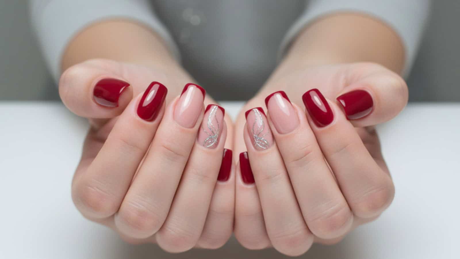 A person displays manicured hands with red and nude nails, featuring silver glitter accents on two nude nails.