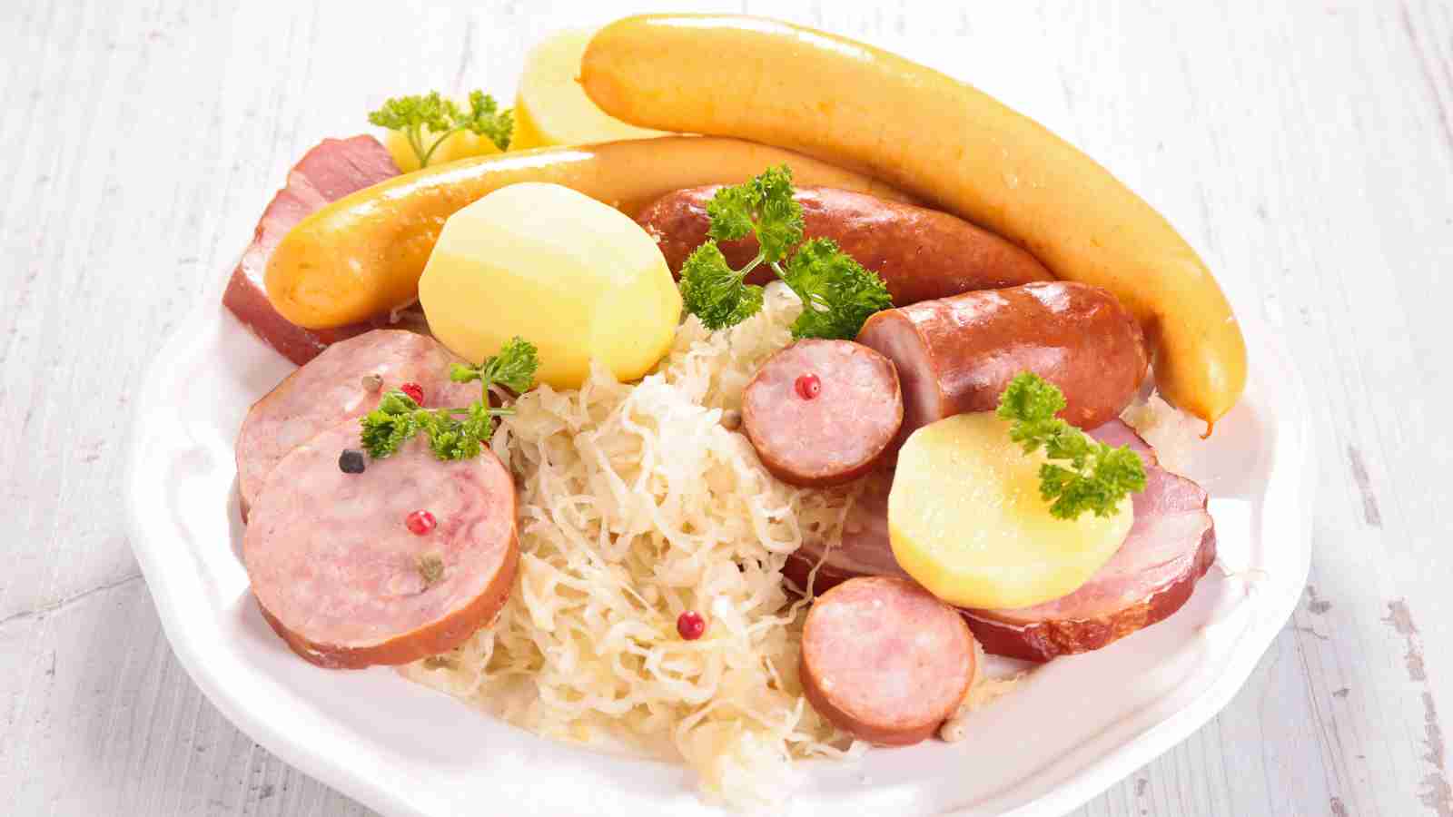 A plate of assorted sausages, boiled potatoes, and sauerkraut garnished with parsley and whole peppercorns.