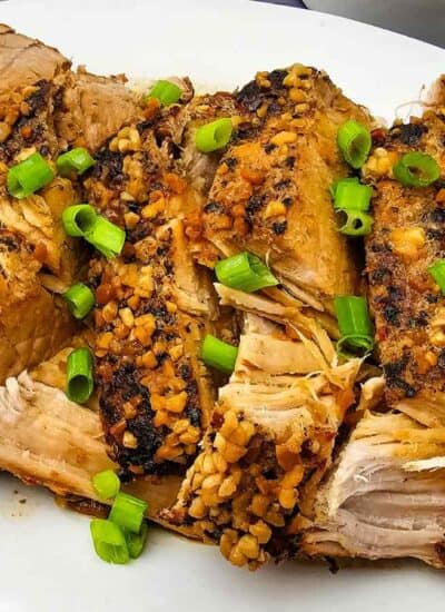 Slices of roasted pork topped with chopped garlic and green onions, arranged on a white oval plate.