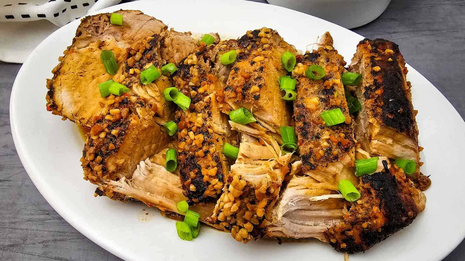 Slices of roasted pork topped with chopped garlic and green onions, arranged on a white oval plate.