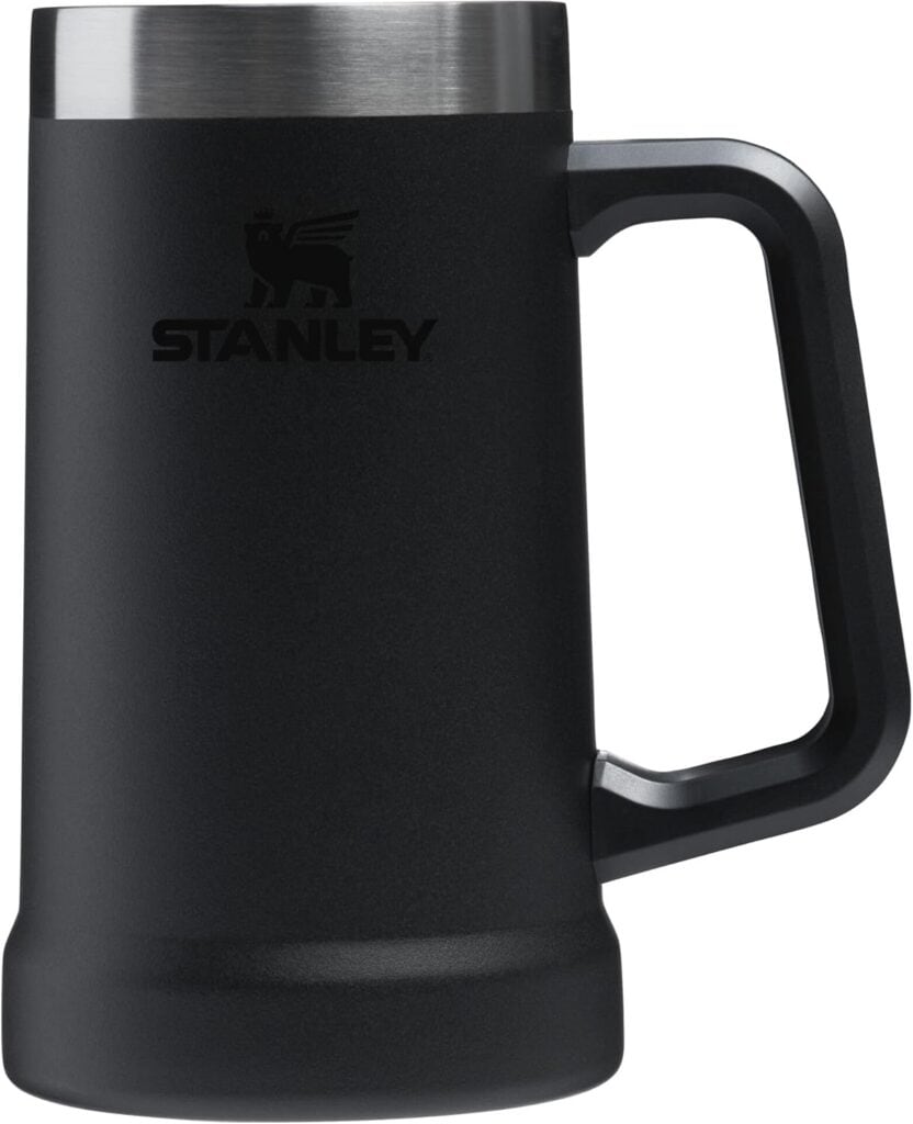 A black Stanley stainless steel mug with a large handle and a silver rim, photographed against a white background.