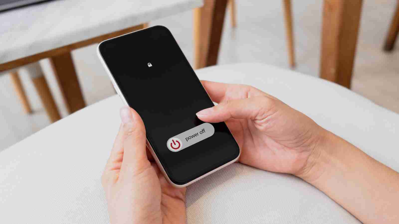 A person holds a smartphone displaying a power off slider, ready to shut down the device.