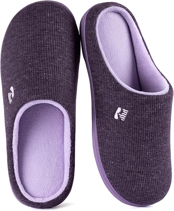A pair of dark purple indoor slippers with light purple interiors, featuring a small white embroidered logo on the upper side of each slipper.