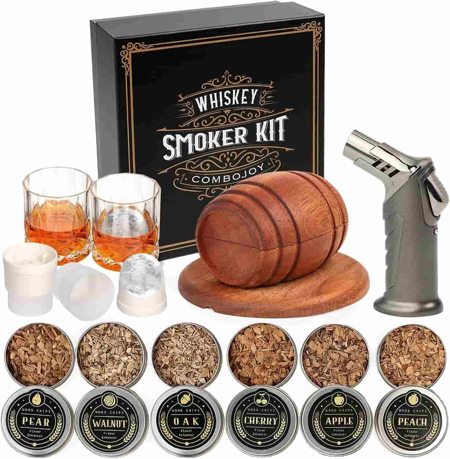 Whiskey smoker kit with two glasses, a wooden smoker, torch, ice molds, and six tins of wood chips in pear, walnut, oak, cherry, apple, and peach flavors, displayed in front of product box.