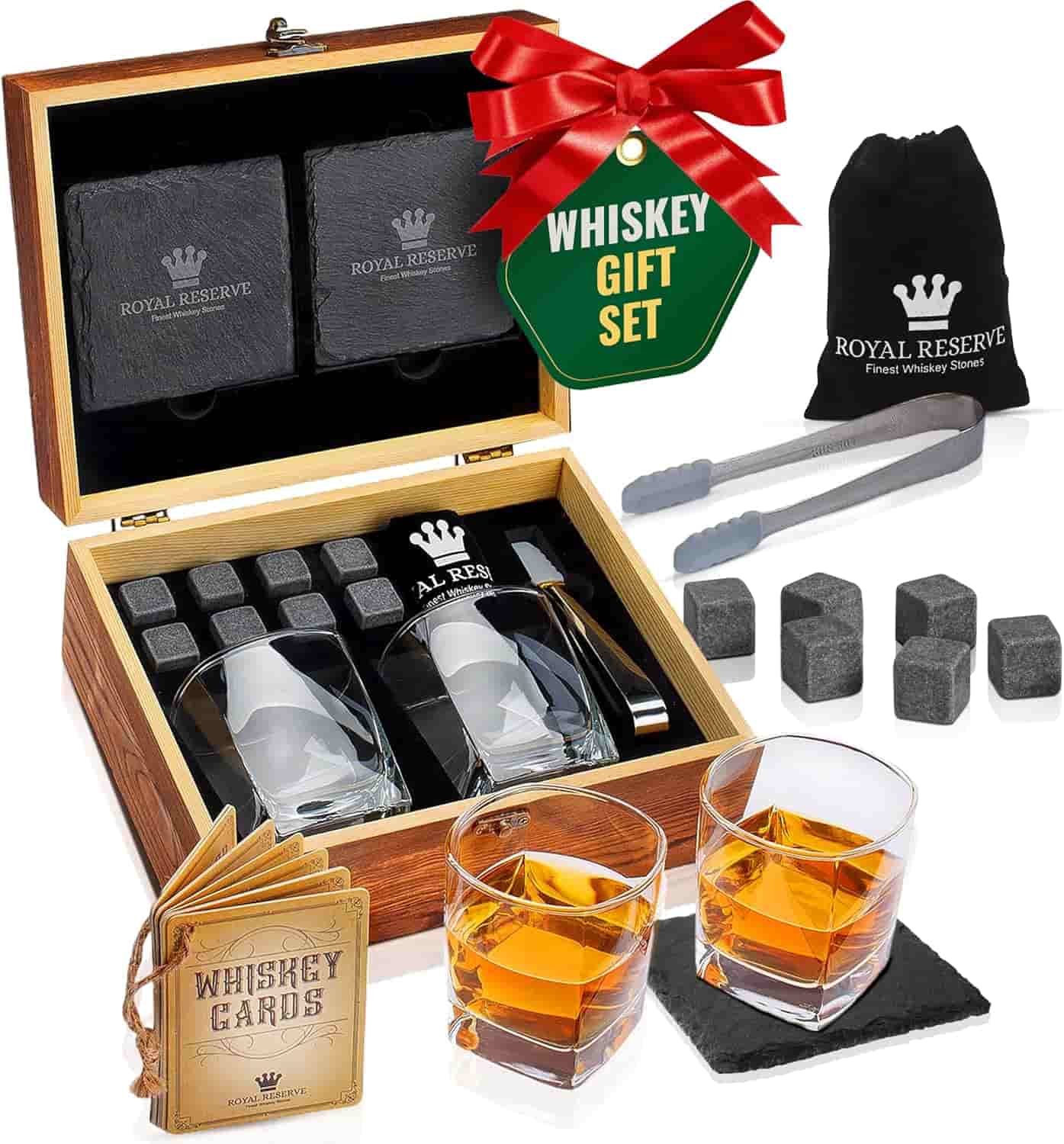 Whiskey gift set with two glasses, whiskey stones, tongs, coasters, whiskey cards, and a wooden box with a red bow and gift tag.