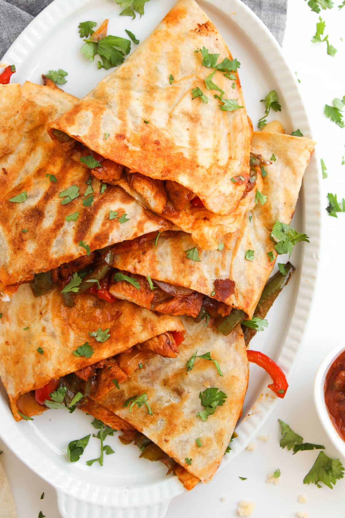 A plate of quesadillas filled with vegetables and topped with chopped cilantro, served with a side of salsa.