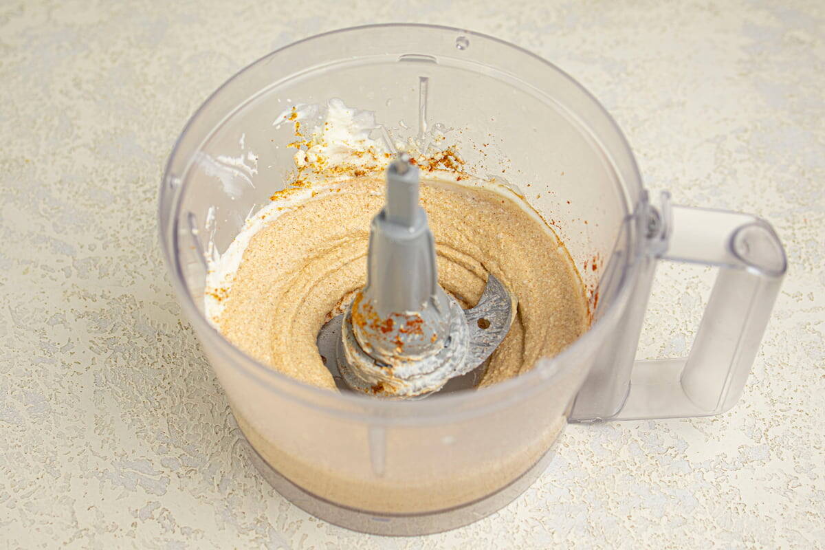 A food processor containing a blended creamy mixture with some spices sprinkled on top, sitting on a light-colored countertop.