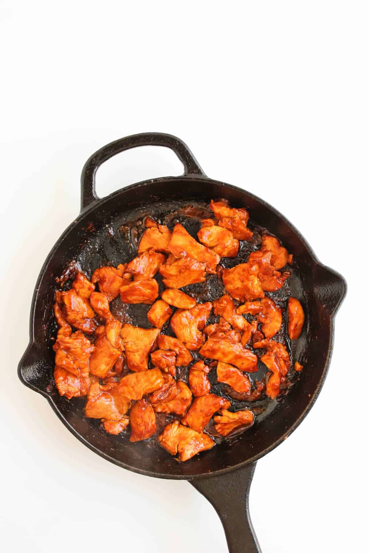 Cooked pieces of marinated chicken in a cast iron skillet on a white background.