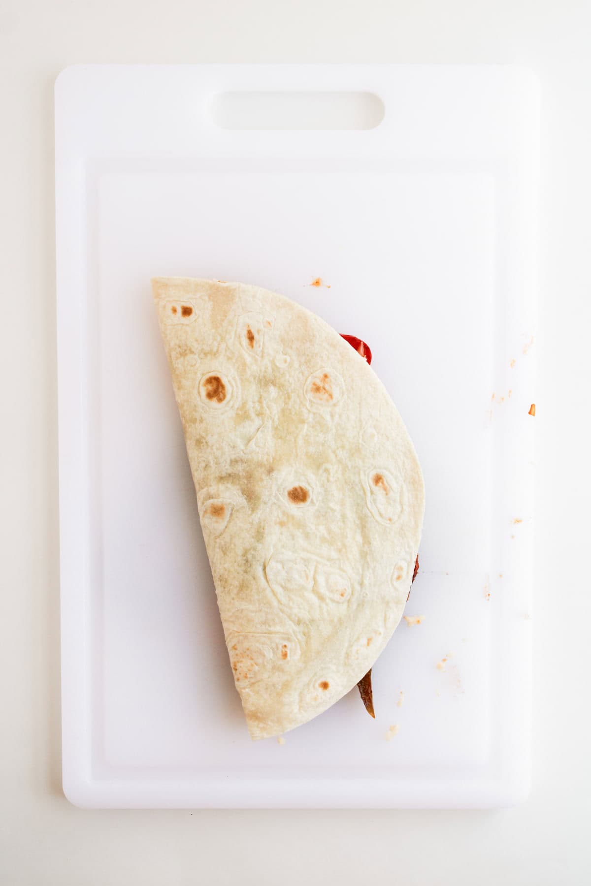 A folded tortilla with visible filling inside sits on a white plastic cutting board.