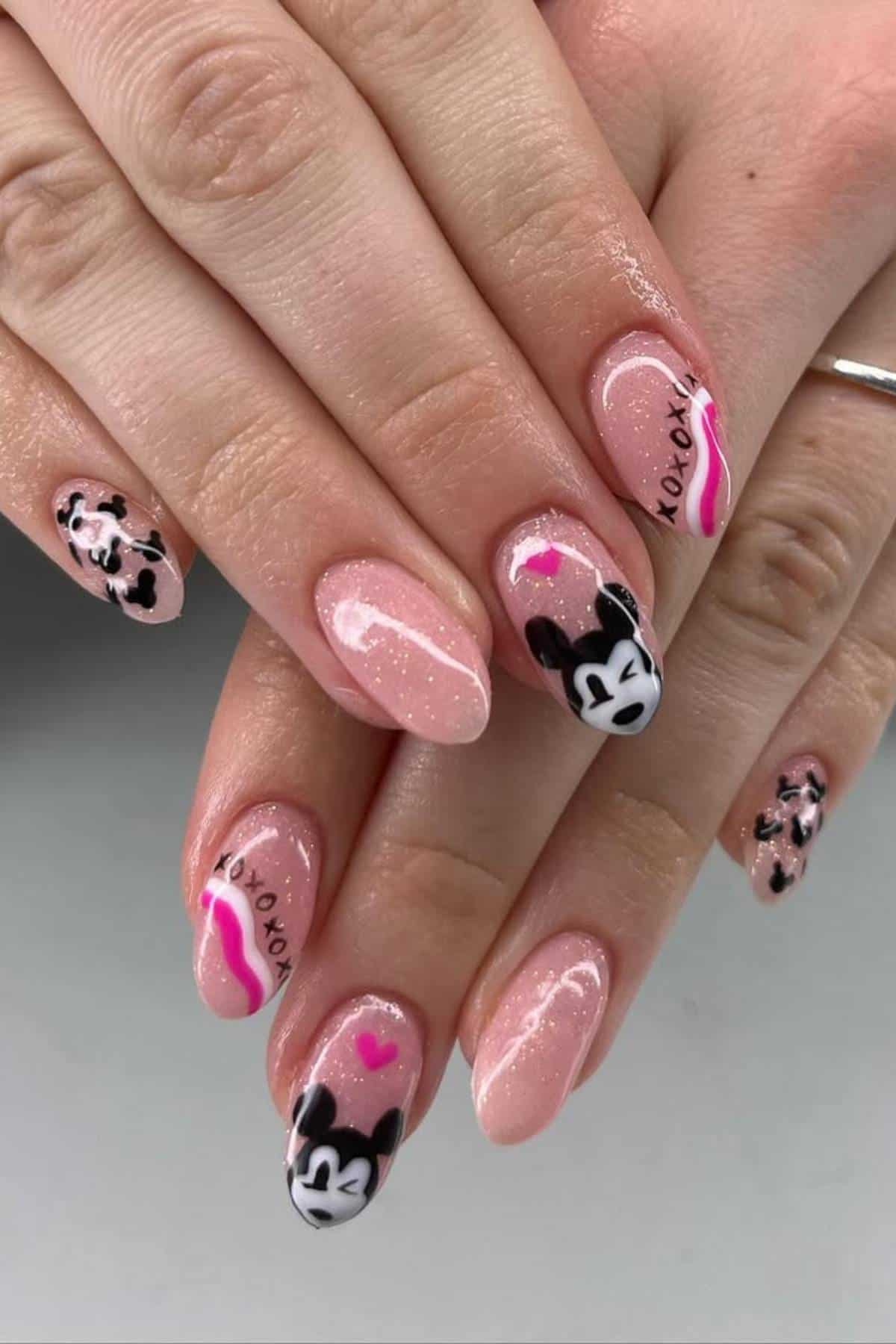 Hands with pink glitter nails featuring black and white cartoon mouse faces, pink hearts, and "xoxo" text designs on several nails.