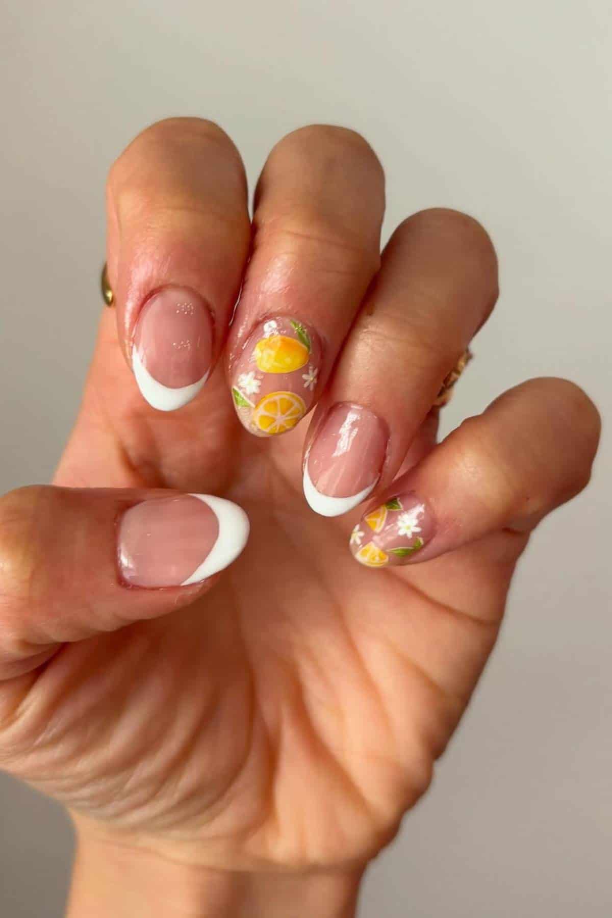 A hand with a French manicure featuring white tips and accent nails decorated with orange and lemon slices and white flowers.