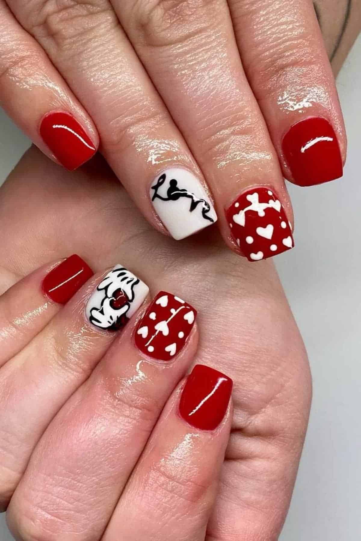 Hands with short, square-shaped nails painted red, featuring white accent nails with heart patterns and black line art designs.