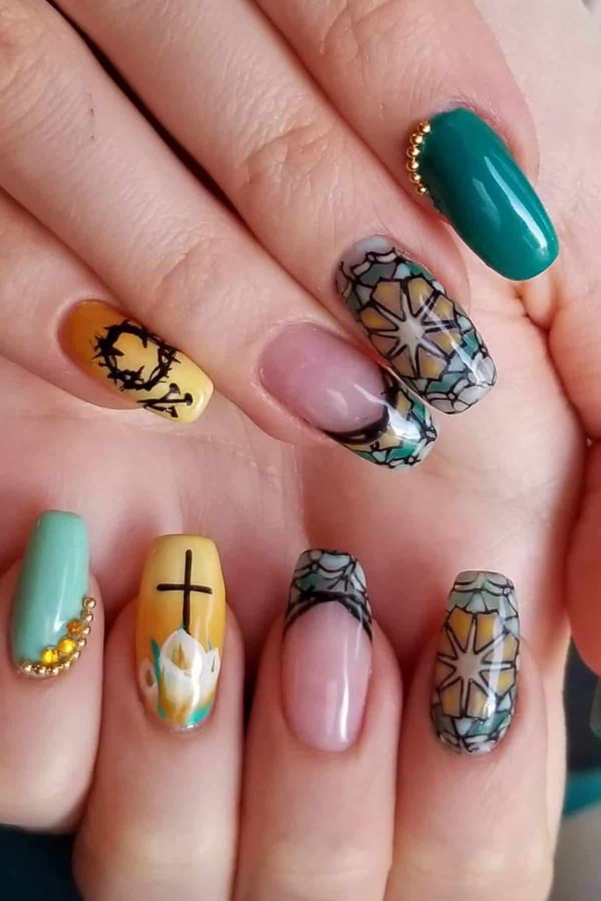 Hands with long, decorated fingernails featuring teal, yellow, and nude tones, with designs including a cross, crown of thorns, geometric patterns, and gold bead accents.